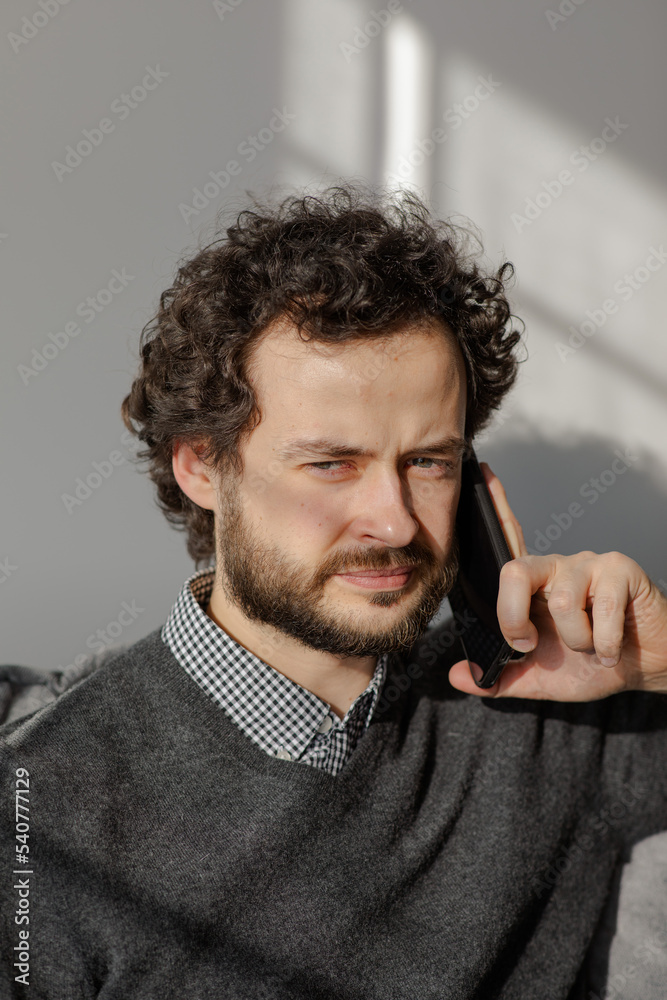 The man is on the phone on the couch..Portrait of a business man who speaks on the phone. Serious young man solves working questions.