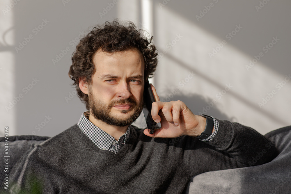 The man is on the phone on the couch..Portrait of a business man who speaks on the phone. Serious young man solves working questions.