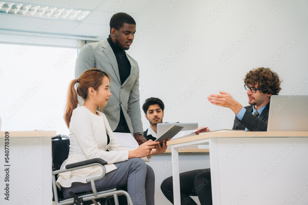 Businesswoman holding a meeting, conference, and conversation with his team while seated in a wheelchair at the workplace. Businesswoman holding a meeting, conference, and conversation with his team while seated in a wheelchair at the workplace.