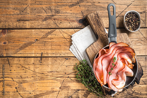 Thinly sliced German Black Forest Ham bacon in skillet. Wooden background. Top view. Copy space