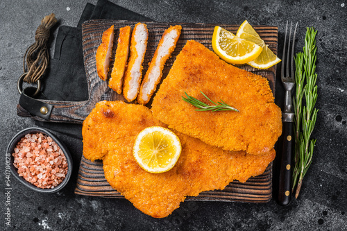 Fried sliced weiner schnitzel on a wooden board with herbs. Black background. Top view