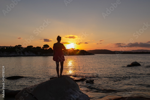 Silhouette of tourist woman holding the sun with panoramic view of sunset over Aegean Mediterranean Sea on Karydi beach, peninsula Sithonia, Chalkidiki (Halkidiki), Greece, Europe. Romantic atmosphere photo