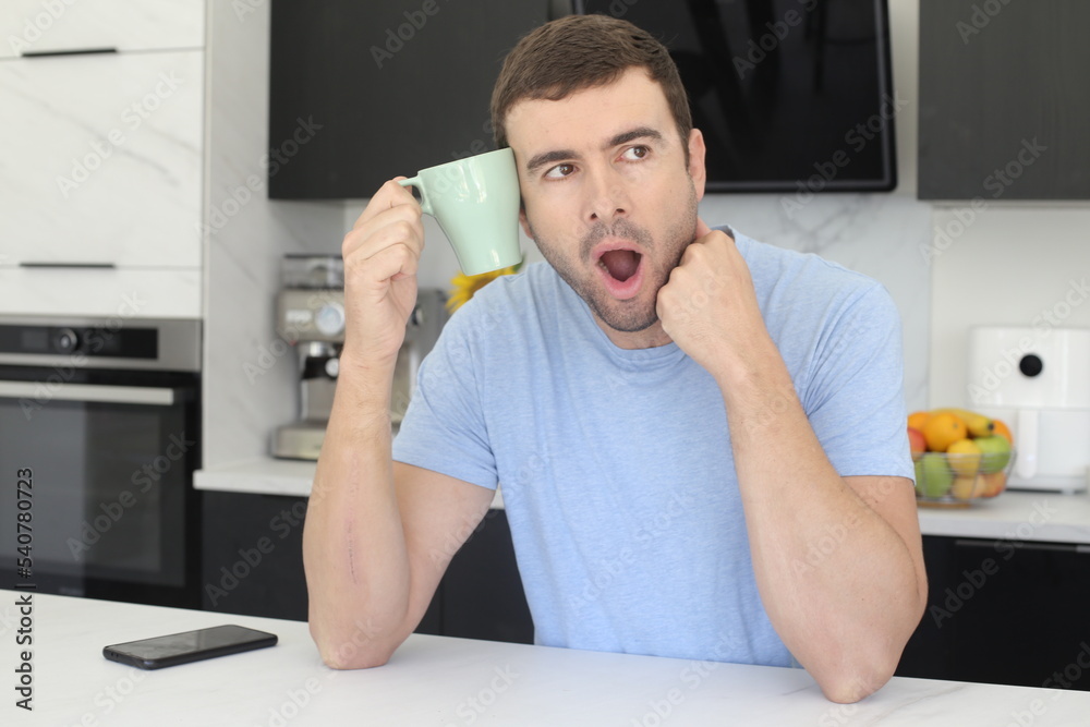 Sleepy looking man holding coffee cup in the kitchen Sleepy looking man holding coffee cup in the kitchen