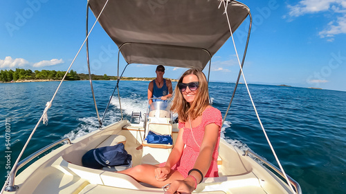 Man driving a luxury rental boat while woman is filming. Near blue lagoon of Vourvourou on peninsula Sithonia, Chalkidiki (Halkidiki), Greece, Europe. Tropical crystals clear turquoise water. Summer