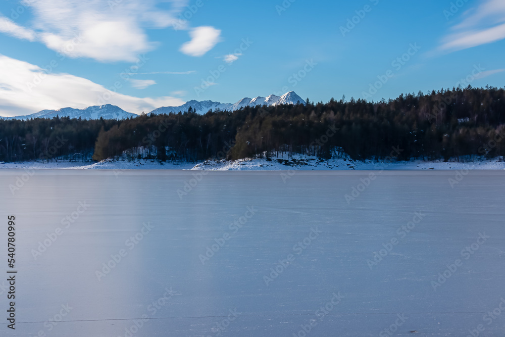 Scenic view of frozen alpine lake Forstsee, Techelsberg, Carinthia (Kaernten), Austria, Europe. Breathing fresh cold air. Winter wonderland. Snow capped Karawanks mountain range, Mittagskogel (Kepa)
