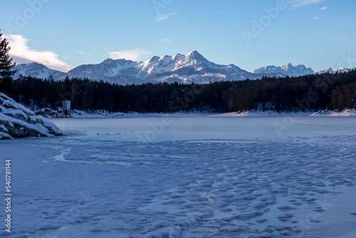 Field of deep crystal snow with scenic view of frozen alpine lake Forstsee  Techelsberg  Carinthia  Kaernten   Austria  Europe. Winter wonderland. Snow capped Karawanks mountains  Mittagskogel  Kepa 