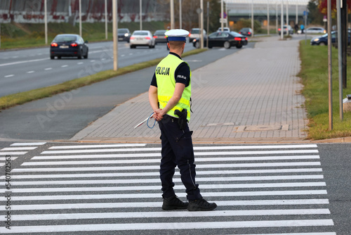 Policjant ruchu drogowego na przejściu dla pieszych kontroluje ruch pieszych. Przy radiowozie. 
