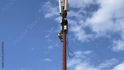 Two workers repairing a cellular tower with blue sky in the background