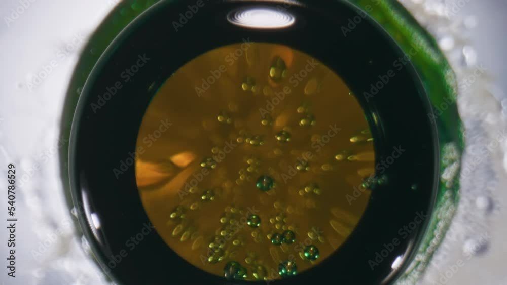 Iced ipa splattering bottle closeup. Golden ale splashing flask slow motion