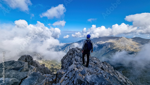 Rear view of man with climbing helmet on cloud covered mountain summit of Mytikas Mount Olympus  Mt Olympus National Park  Macedonia  Greece  Europe. View of rocky ridges and Mediterranean Aegean Sea