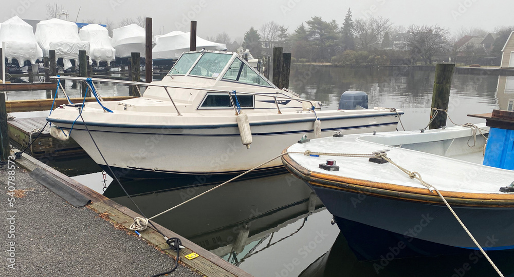 Fototapeta premium Moored boats tied in their boatslip with shrink wrapped boats stored for the winter in the background