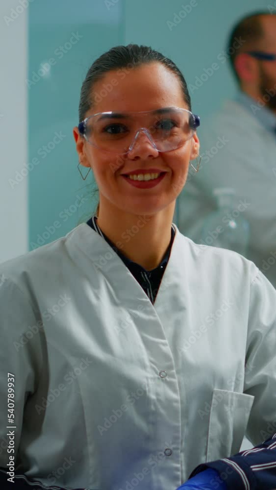 Vertical video: Laboratory doctor looking at camera smiling in modern equipped lab. Multiethnic team examining virus evolution using high tech and chemistry tools for scientific research, vaccine Vertical video: Laboratory doctor looking at camera smiling in modern equipped lab. Multiethnic team examining virus evolution using high tech and chemistry tools for scientific research, vaccine