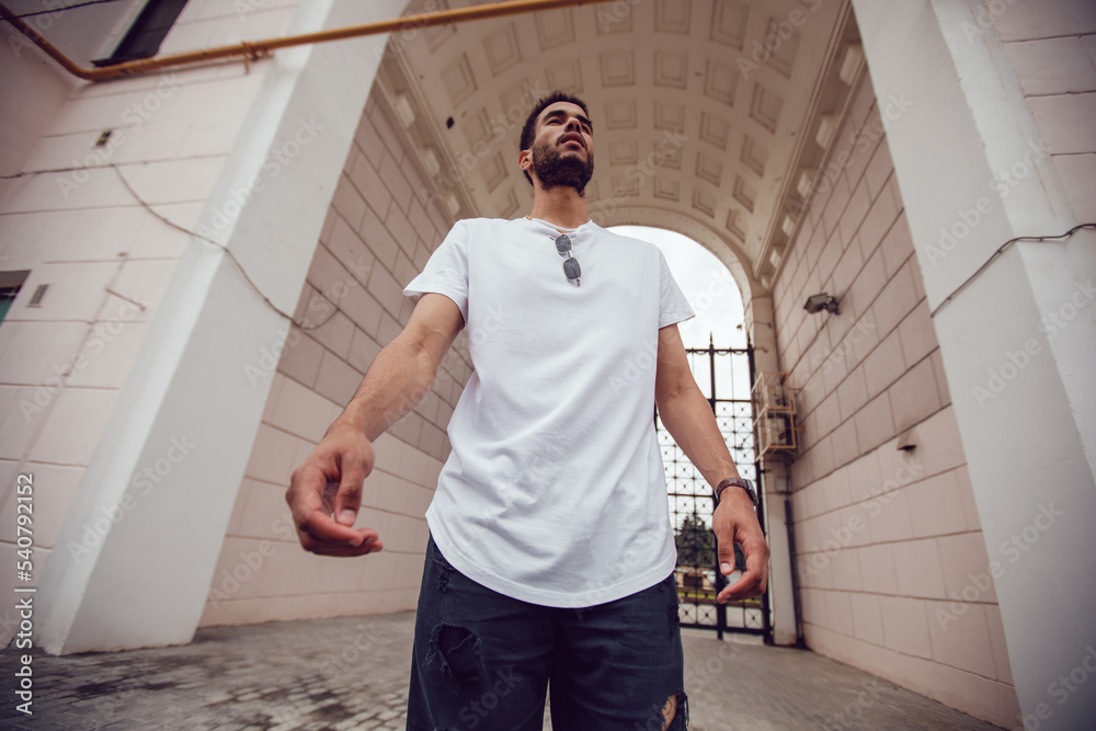 African american man in a white blank t-shirt walks down the street. Mock-up.