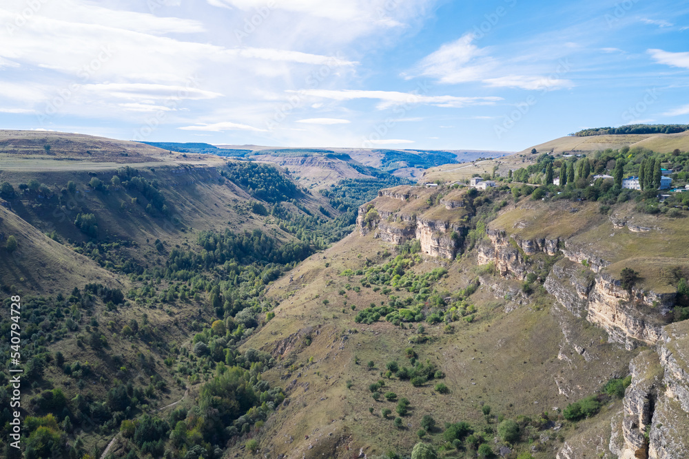 A picturesque winding gorge with a rocky slope. There is a mountain village at the top. Shooting from a drone.