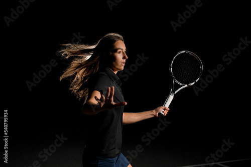 Close-up side view portrait of excited woman with brown flowing hair in black tennis uniform with tennis racket © fesenko