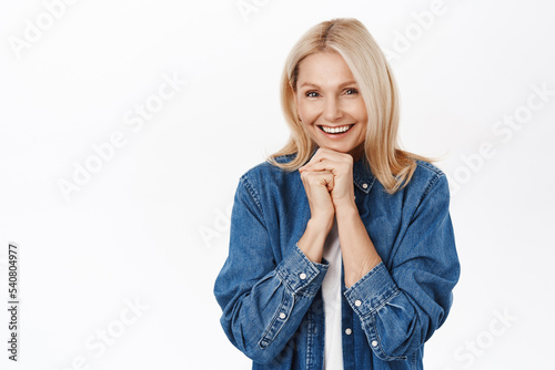 Lovely senior lady looking with love and care at camera, smiling delighted, standing in casual clothes over white background