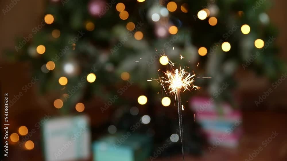 Christmas glittering sparklers candle burns in Christmas tree background. Xmas lighting decoration at home indoor. Festive Magic sparks lights for holiday party. Christmas eve with fireworks