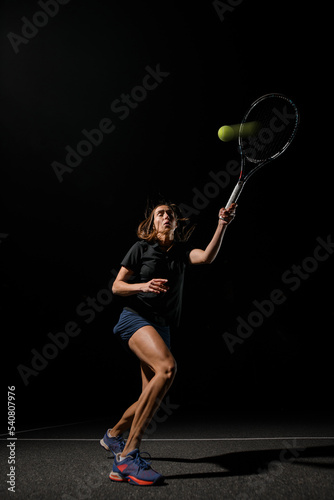athletic woman with tennis racket bleaching yellow tennis ball. Training, practicing in motion, action.