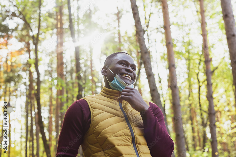 Handsome african american man wearing casual clothes and medical mask smiling happy walking in city park - end of pandemic