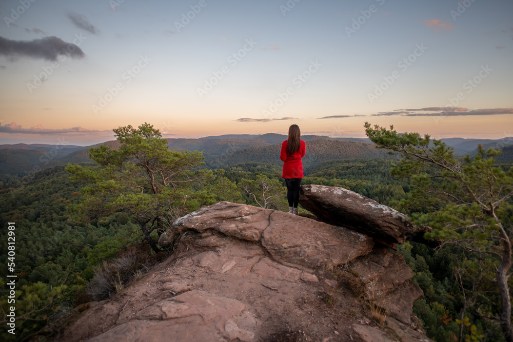 
Eine Frau mit roten Mantel genießt nach der Wanderung, vom Gipfel des Berges, die atemberaubende Aussicht der Landschaft mit einem wunderschönen Sonnenuntergang