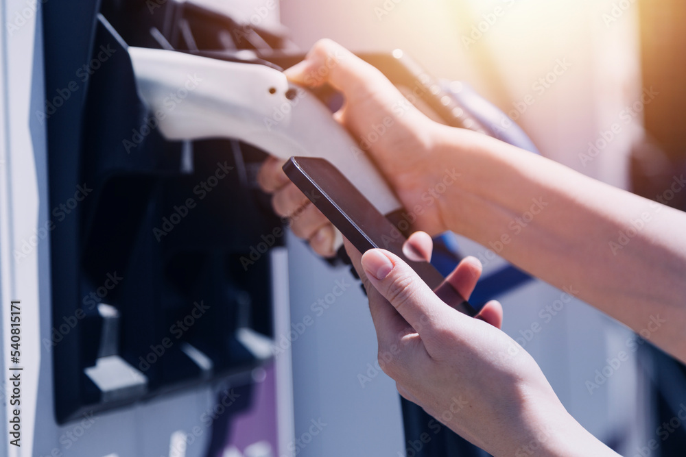 Hand plugging in a charger in an electric car socket.Electric car or ev is charging at station