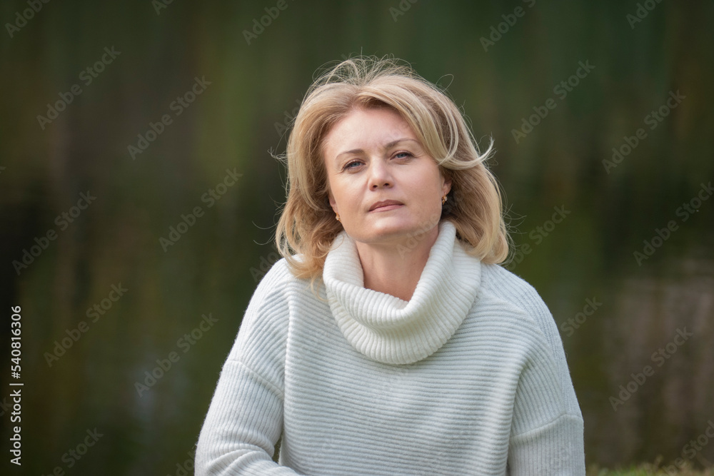 Portrait of serious dreamy European lady concentrated somewhere. Blonde in white sweater against the backdrop of the river looking thoughtfully into the camera. Skepticism. Portrait of serious dreamy European lady concentrated somewhere. Blonde in white sweater against the backdrop of the river looking thoughtfully into the camera. Skepticism.