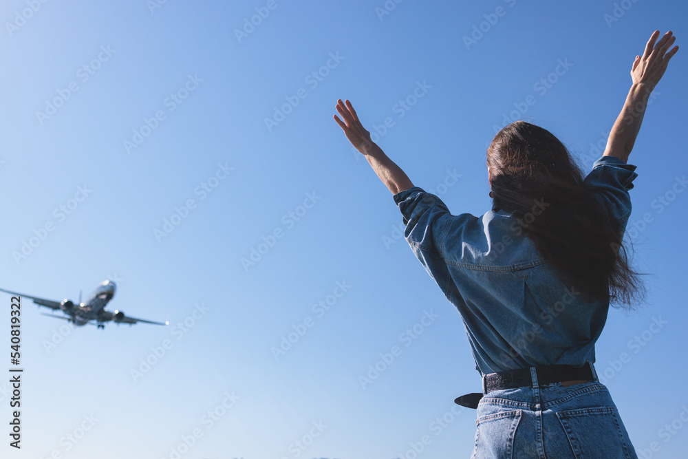 Girl and airplane in flight, landscape with woman standing with hands raised up, waving arms and flying passenger airplane, female tourist and landing commercial aircraft, summer sunny day Girl and airplane in flight, landscape with woman standing with hands raised up, waving arms and flying passenger airplane, female tourist and landing commercial aircraft, summer sunny day