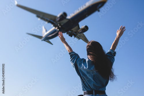 Girl and airplane in flight, landscape with woman standing with hands raised up, waving arms and flying passenger airplane, female tourist and landing commercial aircraft, summer sunny day photo
