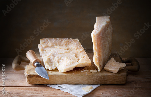 Pieces of parmesan with hard cheese knife on wooden cutting board, space for text, close-up.
