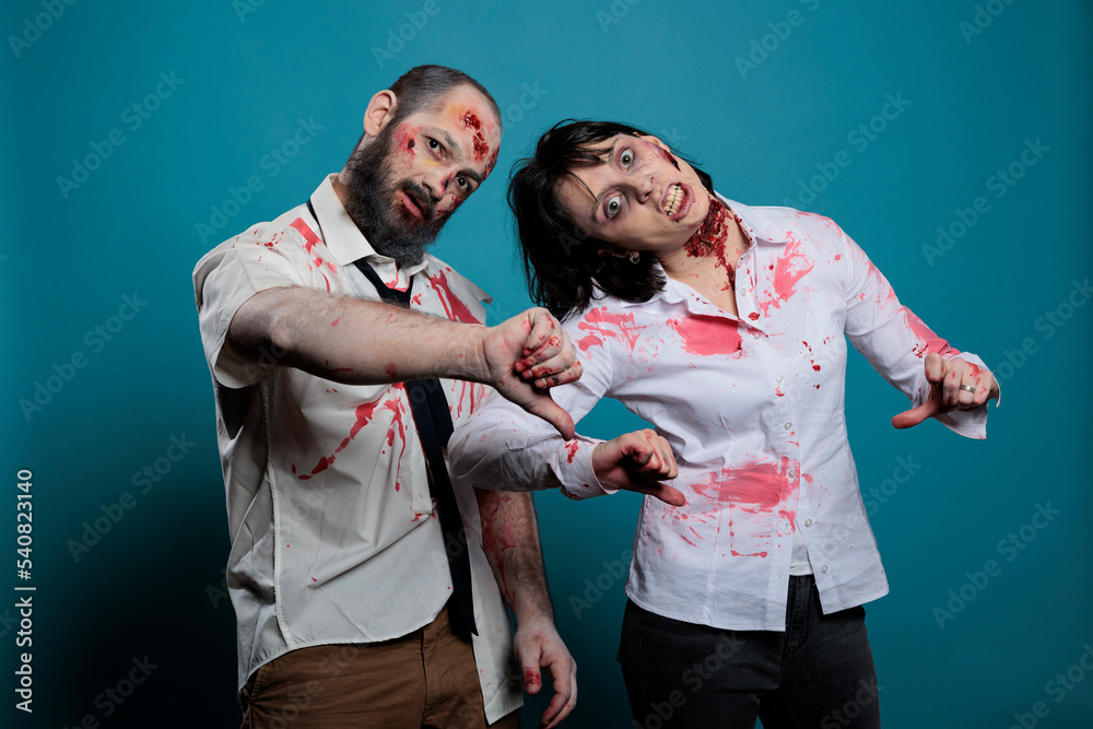 Creepy halloween monsters showing thumbs down on camera, expressing disapproval and dislike in studio. Couple of brain eating zombies with bloody scars and ugly wounds, frightening devils. Creepy halloween monsters showing thumbs down on camera, expressing disapproval and dislike in studio. Couple of brain eating zombies with bloody scars and ugly wounds, frightening devils.