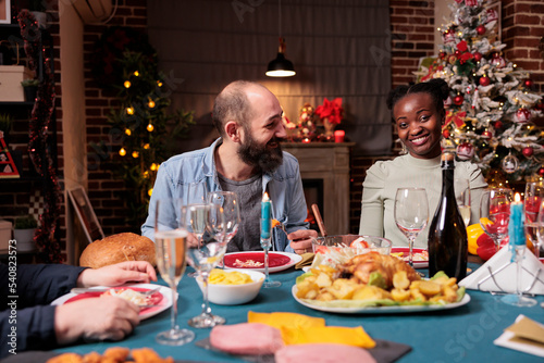 Couple at family christmas holiday celebration, happy friends eating, drinking sparkling wine at festive served dinner table. Man and woman enjoying xmas dishes at home party