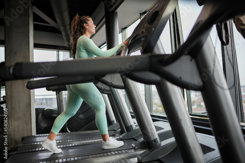 Beautiful cheerful fitness young woman in sportswear running on a treadmill in a fitness center. Sporty beauty at the gym.