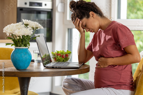 Pregnant woman feeling nauseous in front of laptop