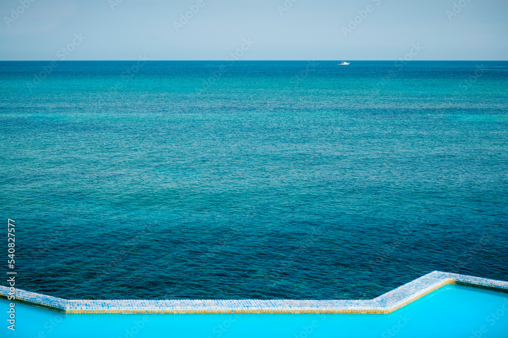 Infinity pool next to the ocean on a blue day. View of the edge of an pool next to the sea during daytime