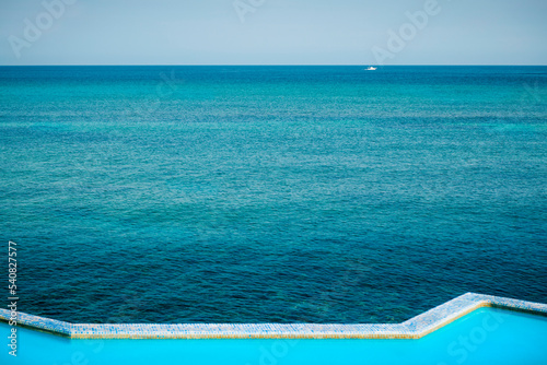 Fototapeta Naklejka Na Ścianę i Meble -  Infinity pool next to the ocean on a blue day. View of the edge of an pool next to the sea during daytime