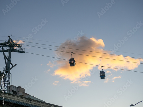 Ropeway. Esaltor booths against the background of a golden cloud. Silhouettes of cable car cabins in the sky.