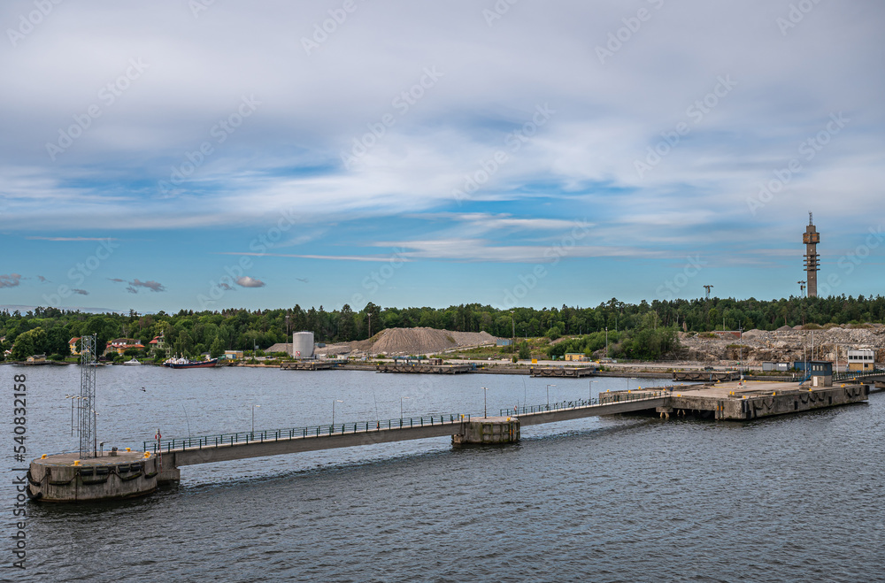 Sweden, Stockholm - July 16, 2022: Ex-Mobil pier with construction site behind in Frihamnen Port. The cookie tower, Kaknästornet, on horizon. Green belt and blue cloudscape