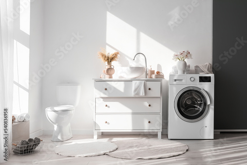 Modern interior of bathroom with washing machine  sink and toilet bowl near white wall