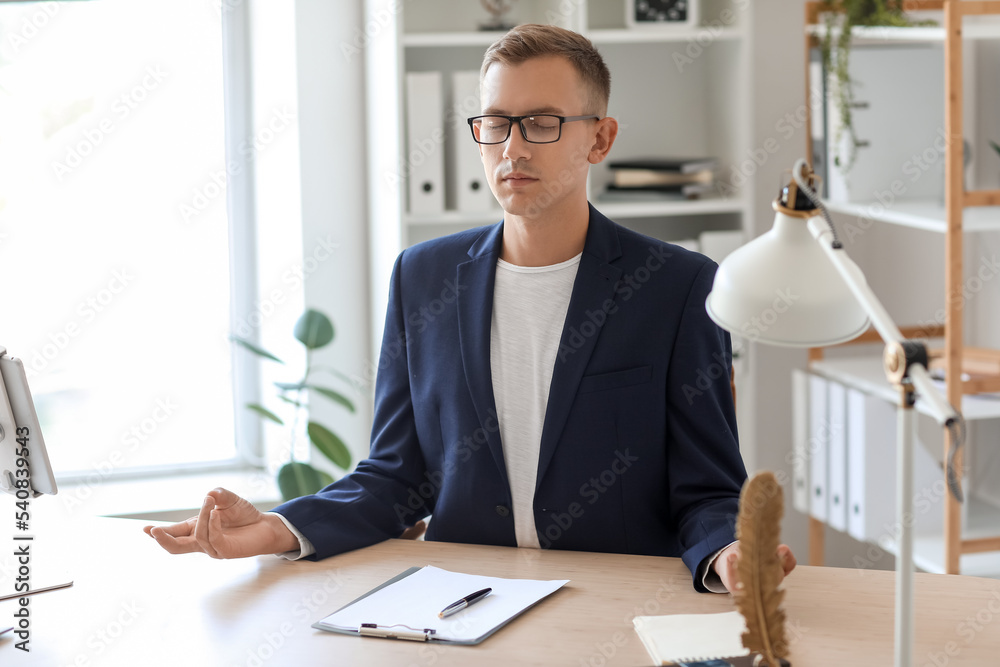 Young man meditating at table in office