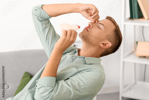 Young man with nosebleed and tissue at home