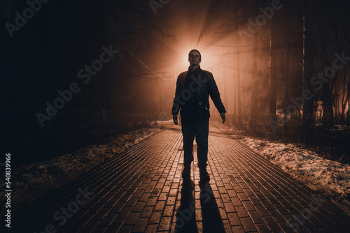 Sad man alone walking along the alley in night foggy park