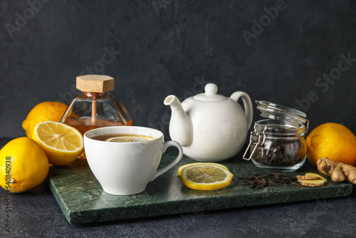 Board with cup of black tea, lemons and teapot on dark background