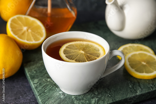 Board with cup of black tea and lemon on dark background, closeup