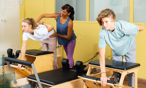 Teen boy and girl in sportswear, pilates training on exercise machine in gym