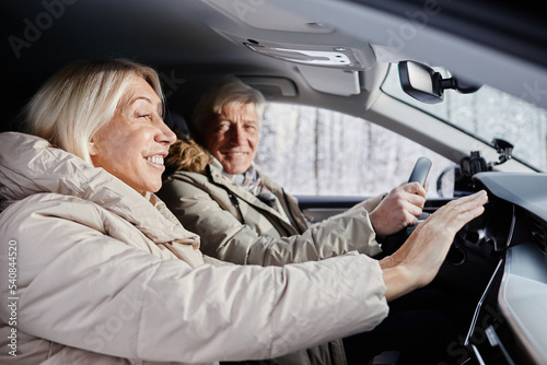 Side view portrait of cheerful senior couple driving car in winter and trying to warm hands on car heater, copy space