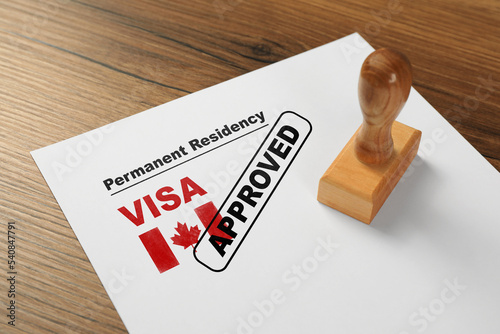 Document with approved permanent residency visa in Canada and stamp on wooden table