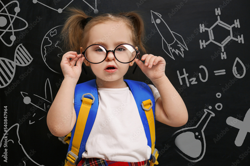 Cute little child wearing glasses near chalkboard with different images