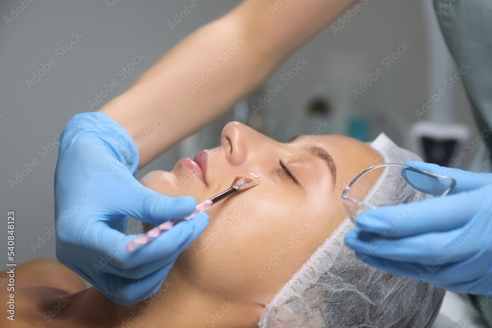Cosmetologist applying chemical peel product on client's face in salon Cosmetologist applying chemical peel product on client's face in salon