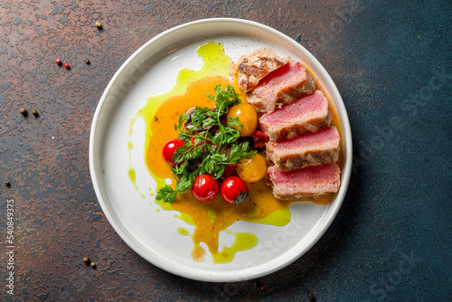 grilled tuna fillet with vegetables on plate on dark stone table top view