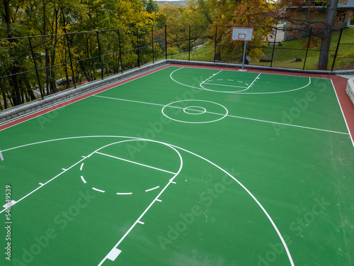 Aerial photo of a green and red outdoor basketball court at school playground.  Court includes retaining walls and black vinyl coated chain link fence.  © Thomas